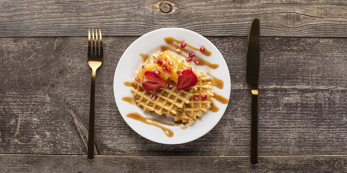 Plate with waffle, icecream and strawberries on wooden plank table and gold knife and fork